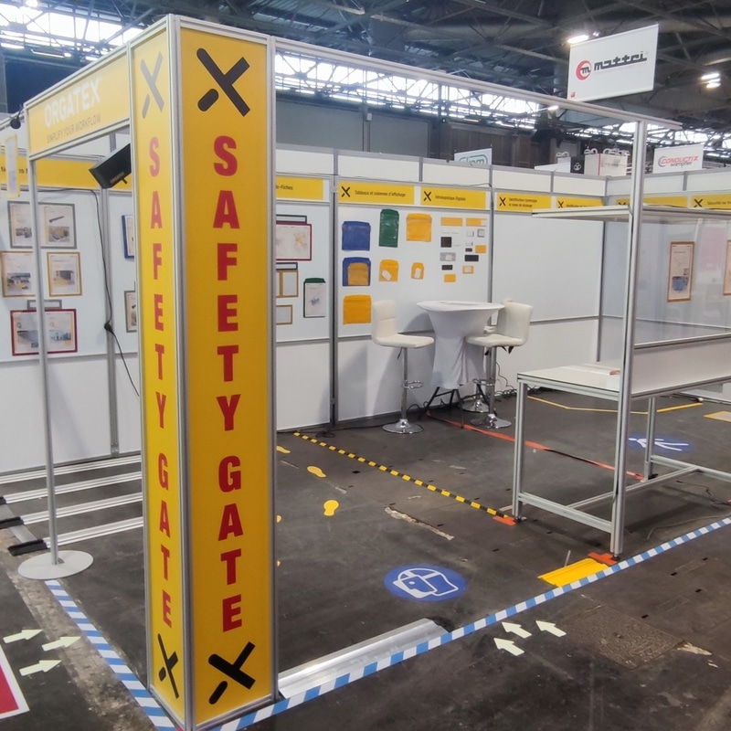 Stand Orgatex Safety Gate : Sécurité Industrielle Salon Stand Orgatex avec pilier jaune Safety Gate et marquages au sol pour la sécurité industrielle en entreprise.